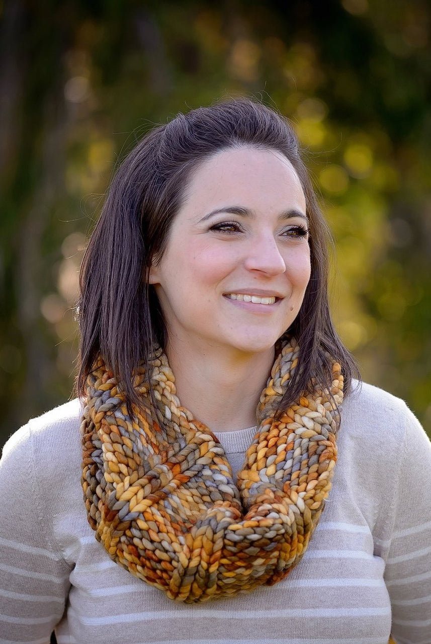 A portrait shot of a woman wearing the Slouch Cowl in the Laguna Negra colourway, standing in front of a backdrop of trees