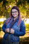A smiling woman with pink hair wears a Triangulate cowl in the 'Plomo' colourway tucked inside their jean jacket.